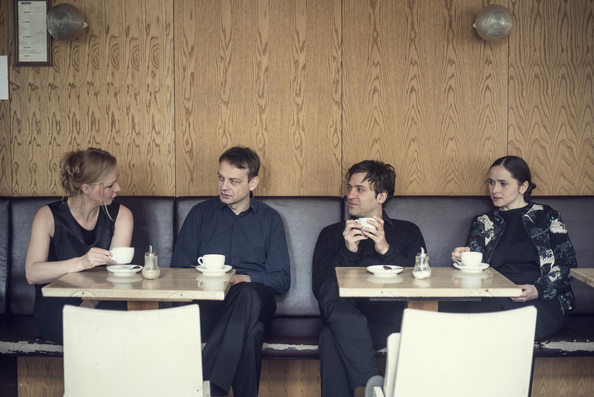 Die vier Mitglieder des Ensemble Adapter sitzen einer holzvertäfelten Bar und trinken Kaffee.