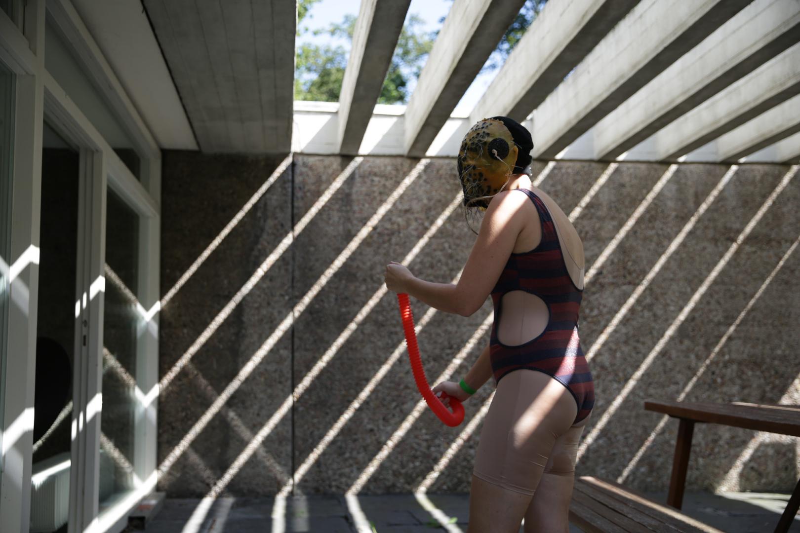 Performance draussen im Hof der Akademie der Künste, die Performerin trägt Badeanzug und Maske 