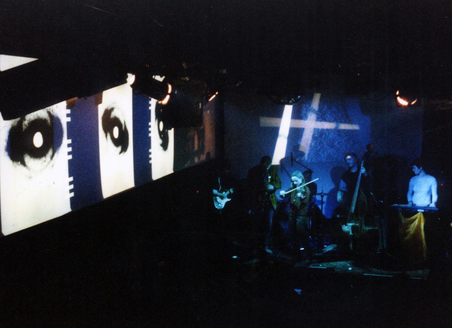 Eine Aufnahme aus der Maria am Ostbahnhof, links Videoprojektionen, rechts die Band und im Vordergrund das Publikum